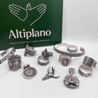 Une collection de bijoux artisanaux en argent de la boutique Altiplano, mettant en valeur des textures et motifs inspirés de l'art latino-américain, comprenant des bagues, des bracelets et des pendentifs devant un fond vert avec le logo Altiplano.