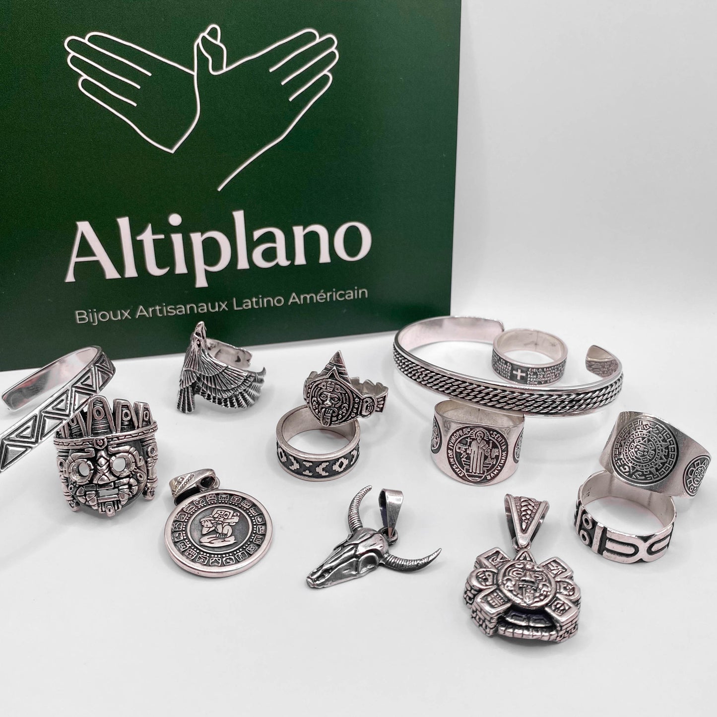 Une collection de bijoux artisanaux en argent de la boutique Altiplano, mettant en valeur des textures et motifs inspirés de l'art latino-américain, comprenant des bagues, des bracelets et des pendentifs devant un fond vert avec le logo Altiplano.