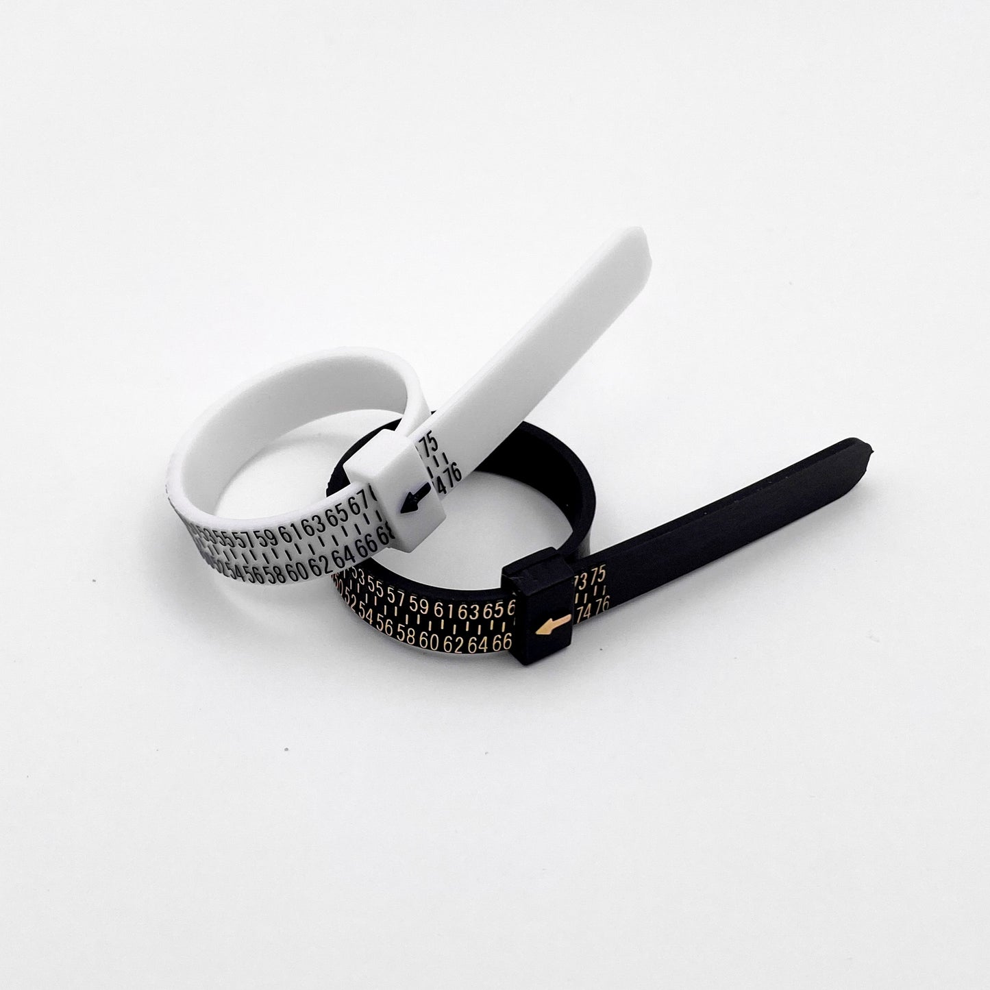 Photo de deux baguiers (Anneaux de mesure pour les tailles de bague) de couleur noire et blanche posés côte à côte sur un fond blanc. Les baguiers affichent des graduations de taille en chiffres dorés et noirs, avec une petite flèche indiquant la taille. Produit par la boutique de bijoux en argent "Altiplano".