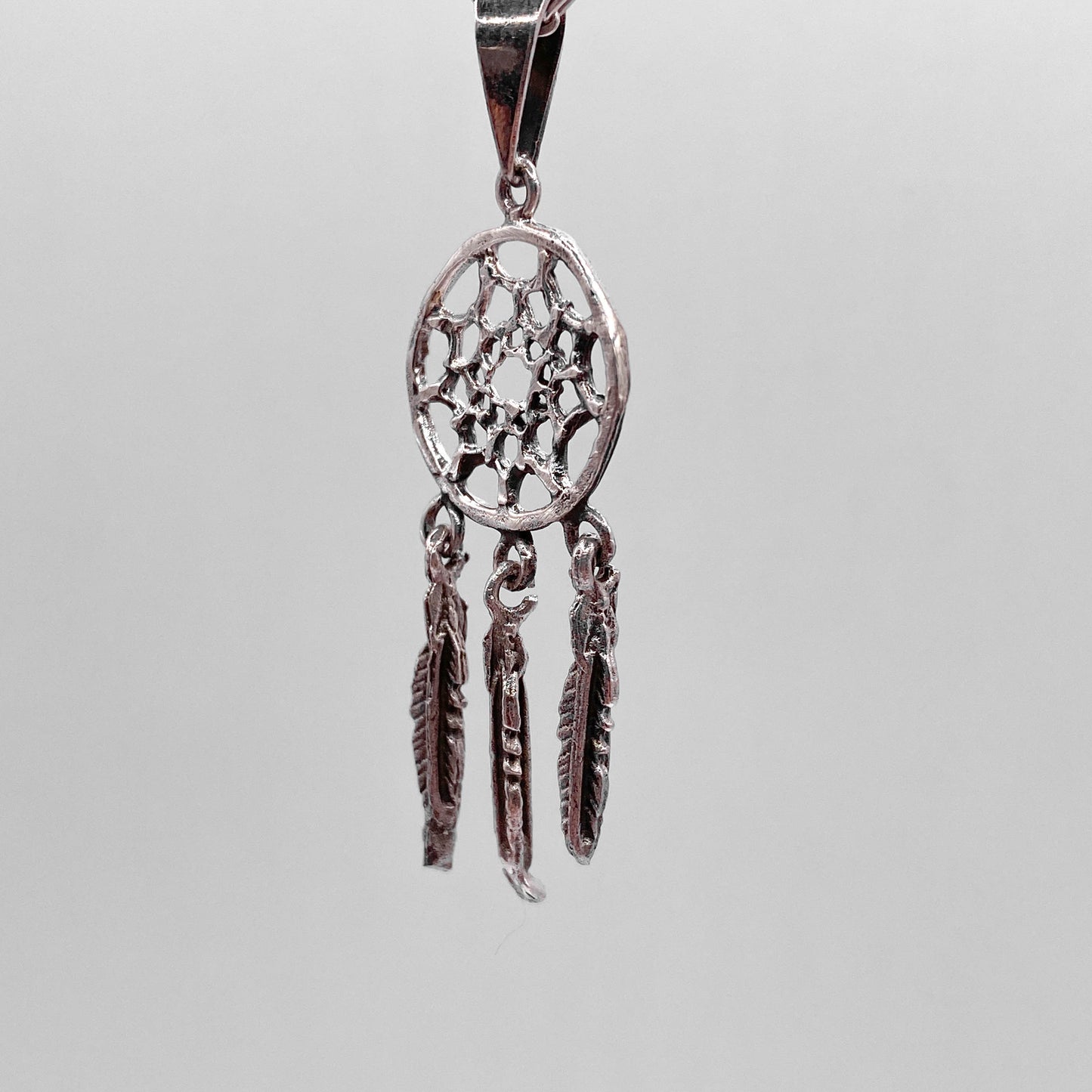 Médaillon en argent représentant un capteur de rêves avec trois plumes suspendues. Le design est finement ciselé, combinant inspiration traditionnelle et artisanat latino-américain. Disponible dans la boutique en ligne Altiplano.