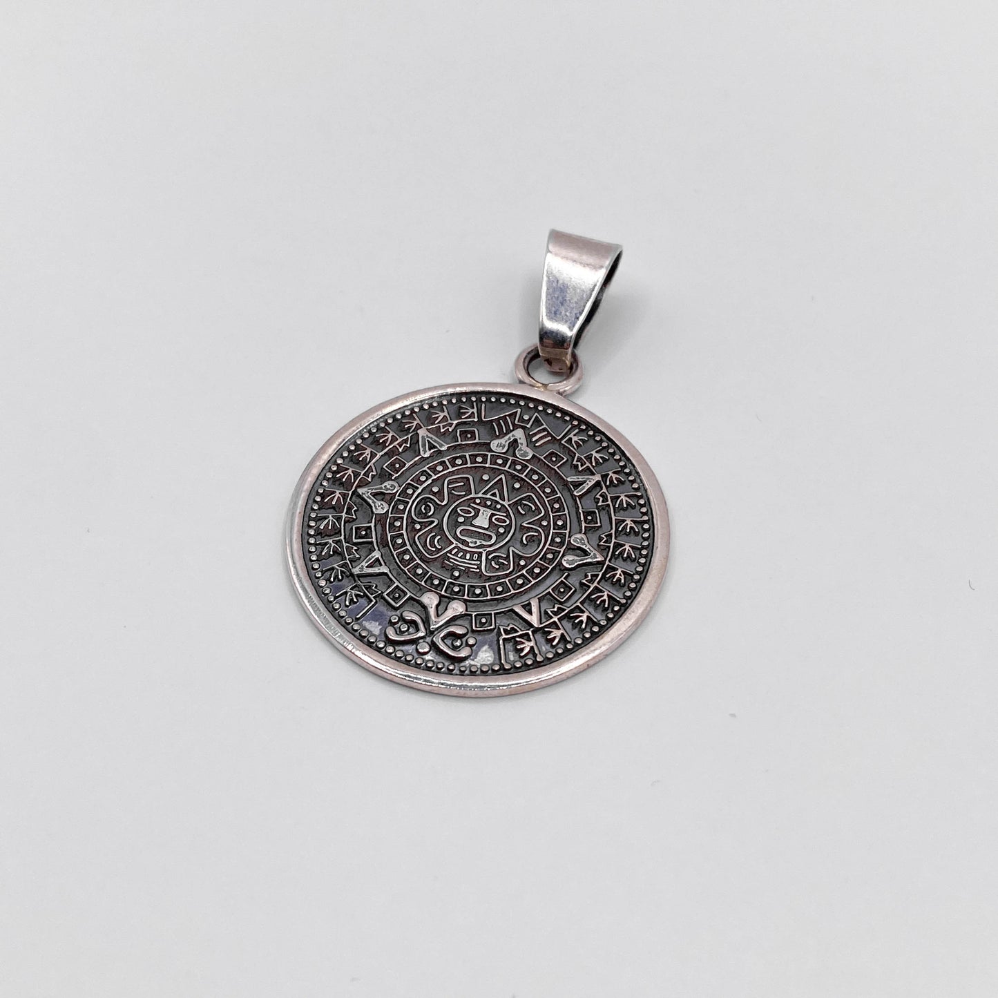 Pendentif rond en argent finement gravé représentant un calendrier aztèque, disponible dans la boutique Altiplano.