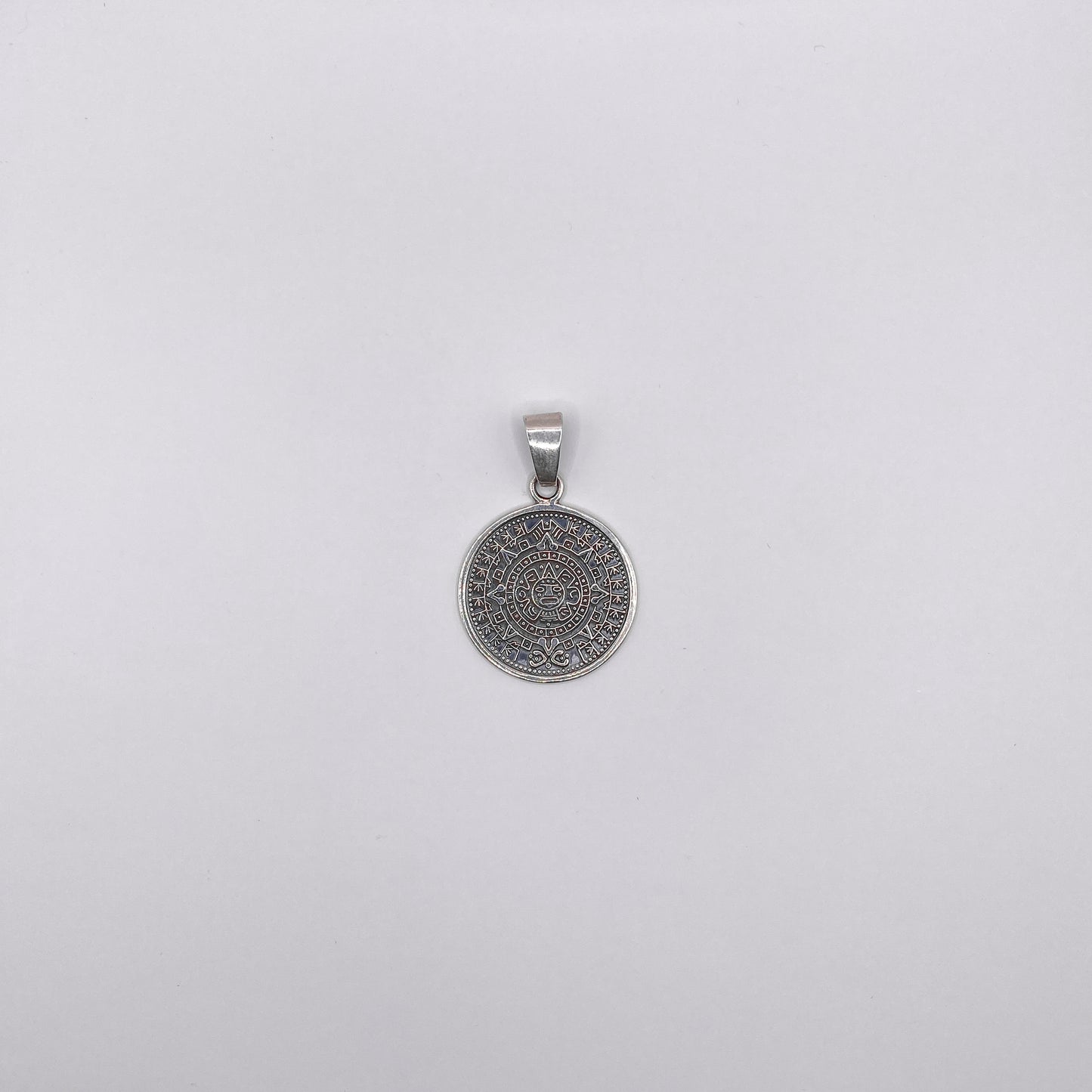 Un pendentif rond en argent finement ciselé, représentant un motif aztèque détaillé, disponible sur la boutique en ligne de bijoux Altiplano.