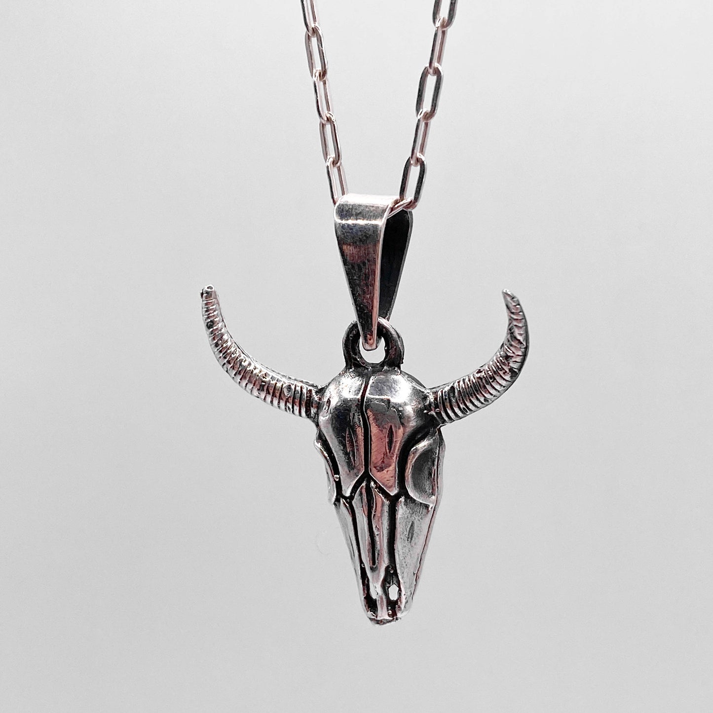 Un collier en argent avec un pendentif en forme de tête de bison ornée de cornes, proposé par la boutique de bijoux latino-américains "Altiplano". Le design détaillé et le métal poli confèrent une allure unique et artisanale à ce bijou intitulé "MICTLAN".
