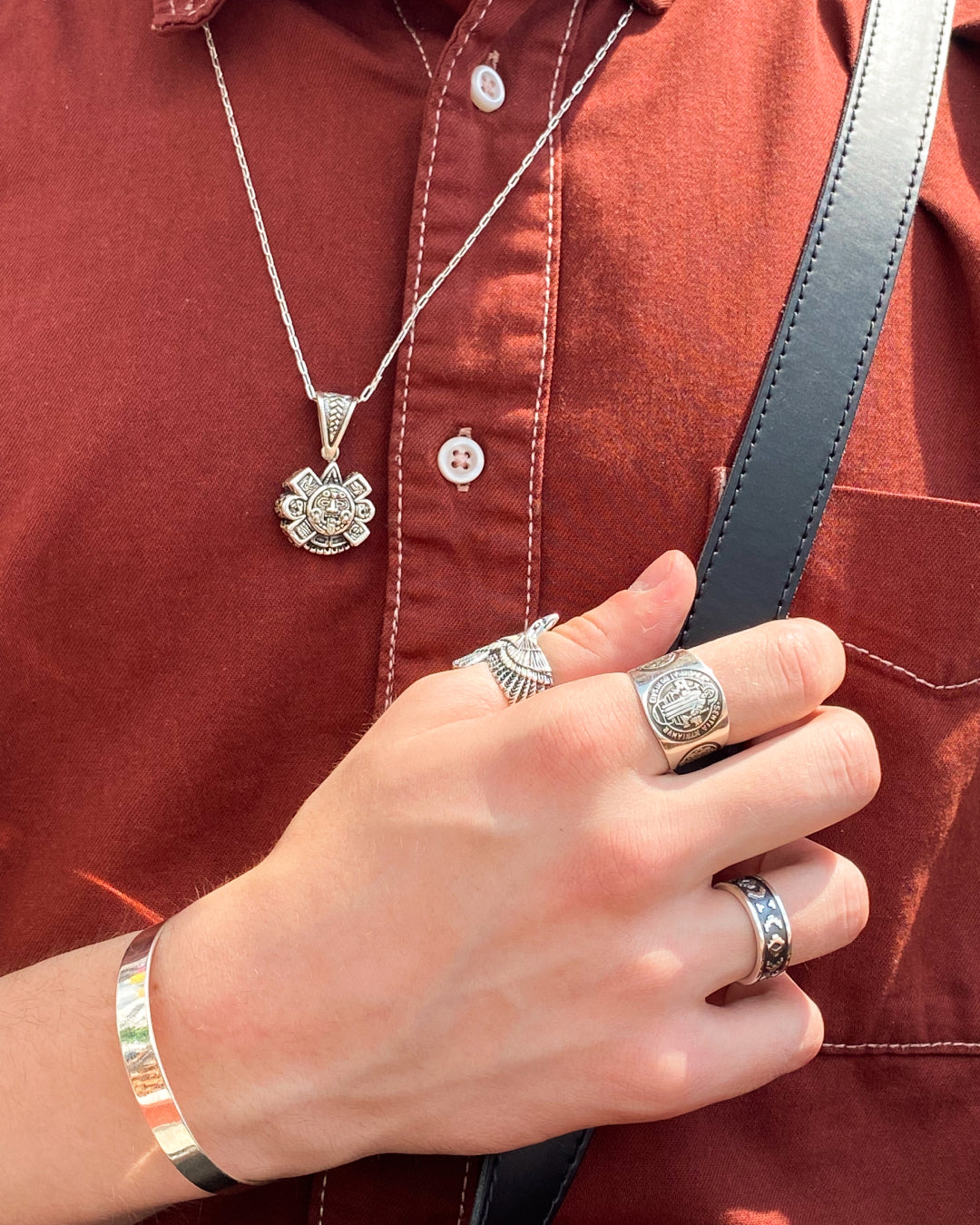 Un homme portant des bijoux en argent, notamment une chaîne avec un pendentif gravé, trois bagues massives et un bracelet simple. Élégance et artisanat latino-américains disponibles chez Altiplano.