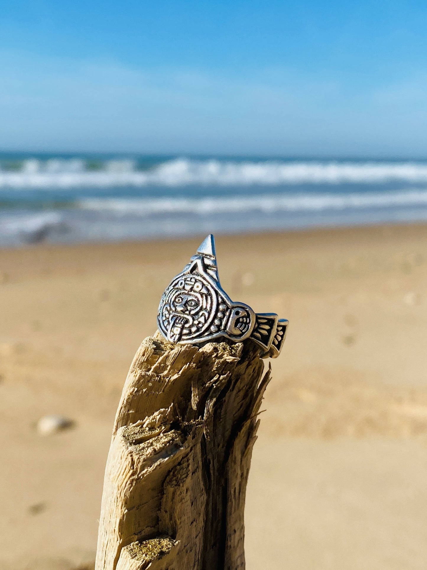 Bague en argent Tonatiuh avec motifs aztèques, montée sur un morceau de bois en bord de mer, disponible sur la boutique en ligne Altiplano pour des créations de bijoux latino-américains uniques.