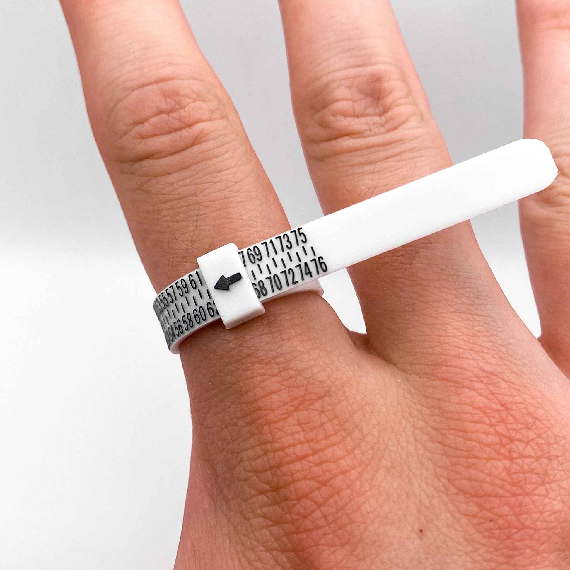 Image montrant un baguier réglable en plastique blanc autour d'un doigt, utilisé pour mesurer la taille des bagues. Produit proposé par la boutique en ligne "Altiplano", spécialisée dans les bijoux en argent latino-américains.